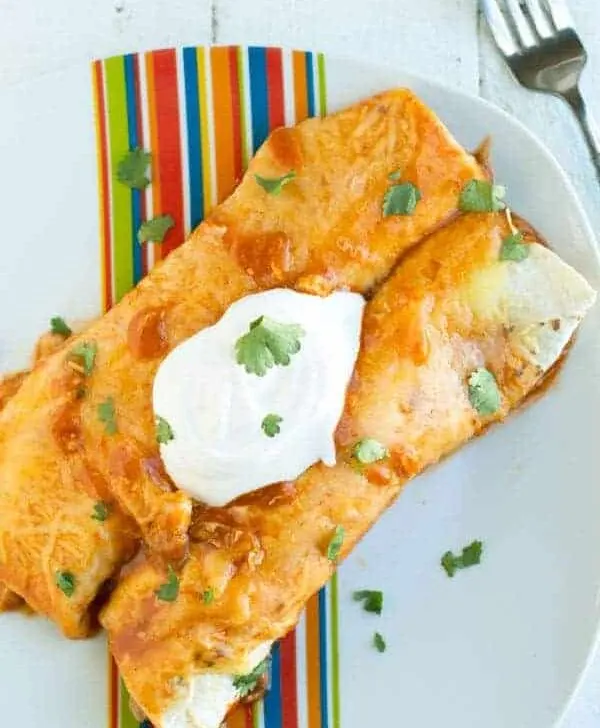These easy chicken enchiladas are stuffed with slow roasted chicken and refried beans and topped with spicy enchilada sauce and melted cheese.